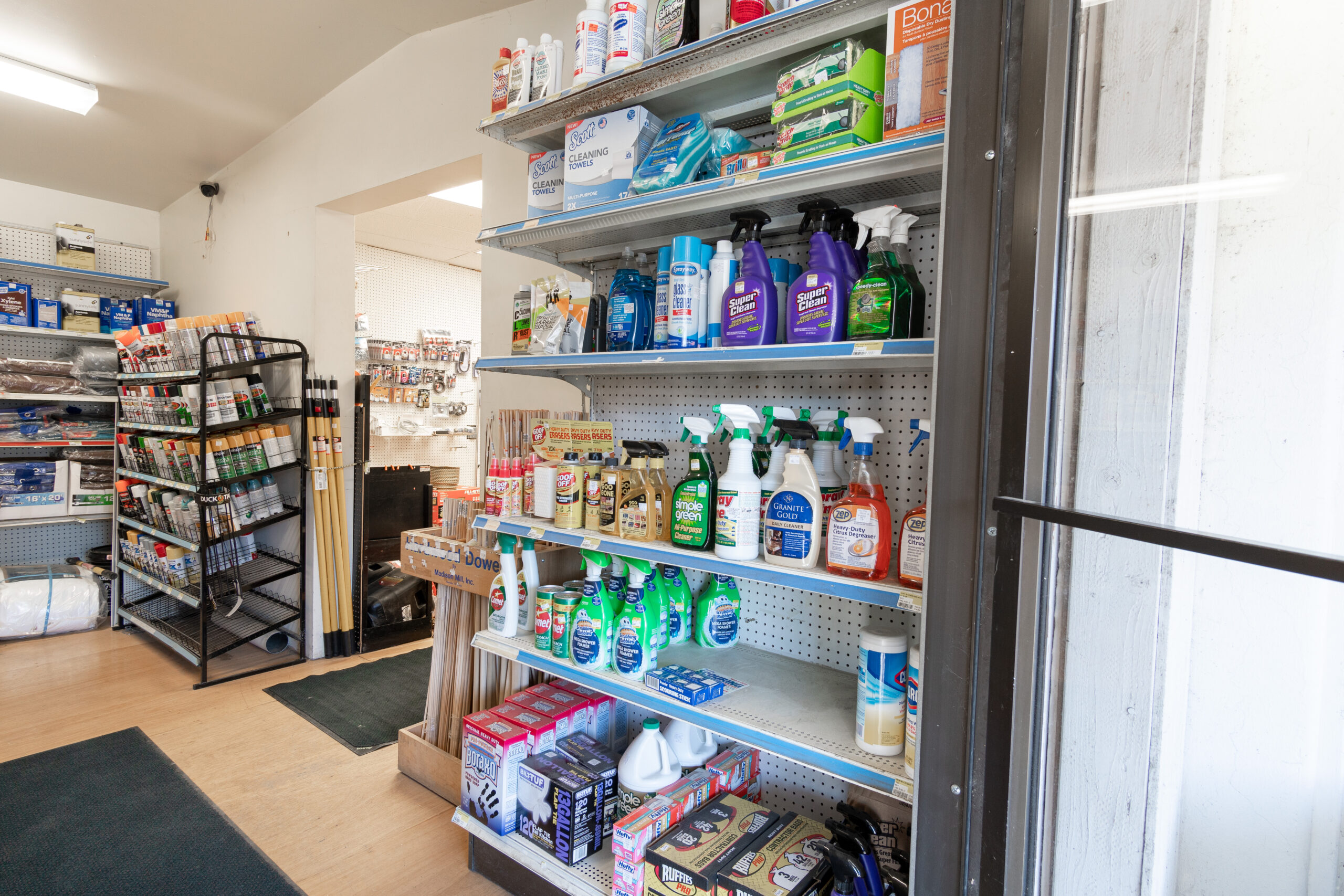 A shelf in Four Star Supply, full of cleaning supplies like glass cleaner, paper towels, trash bags, wet wipes, & other products.