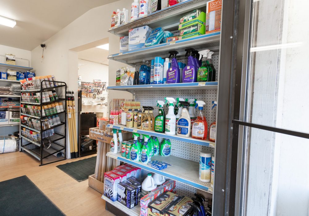 A shelf in Four Star Supply, full of cleaning supplies like glass cleaner, paper towels, trash bags, wet wipes, & other products.